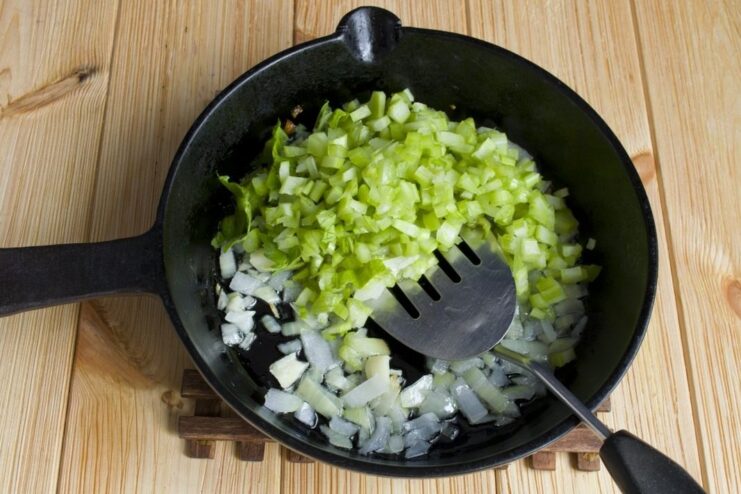 Adding finely diced celery to the sautéed onion in the pan. Diced celery being added to the pan with sautéed onions.