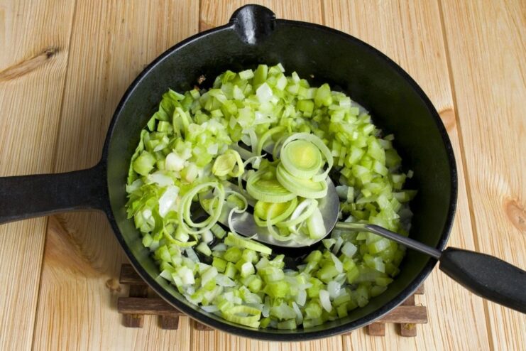 Adding sliced leek to the pan and stewing the vegetables until soft. Sliced leek being added to the celery and onion mixture in the pan.