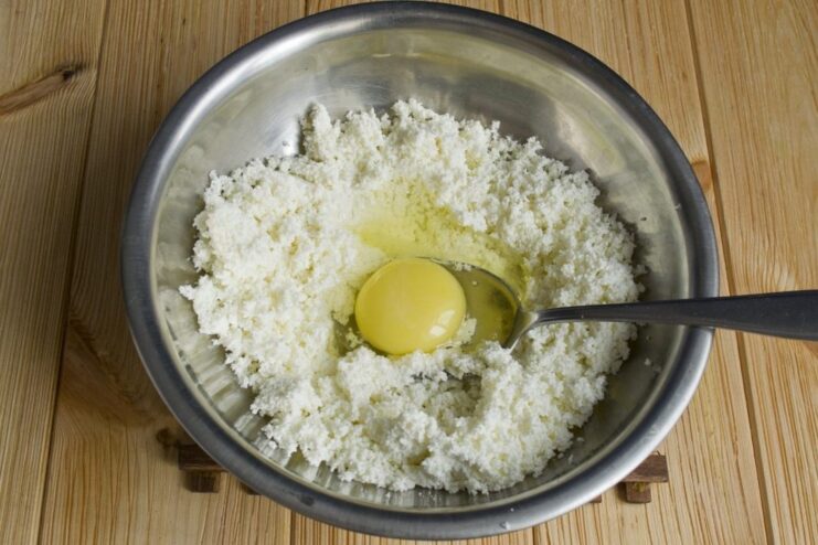 Mixing the sifted farmer's cheese with an egg and a pinch of salt. An egg and salt being added to the bowl of sifted farmer's cheese.