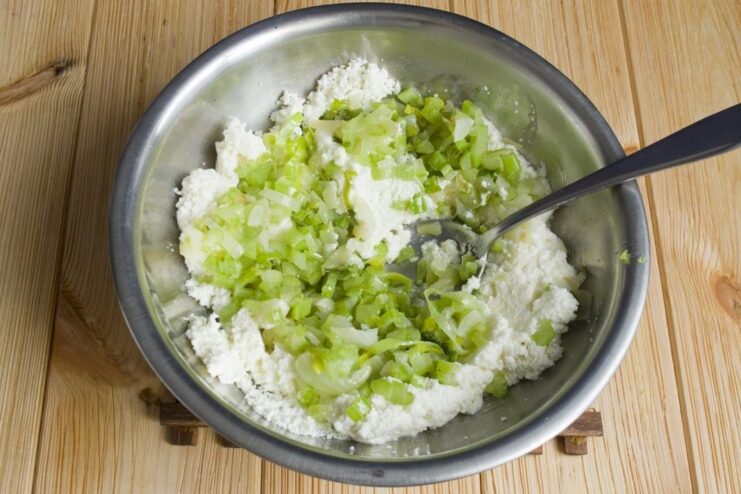 Combining the cooled sautéed vegetables with the farmer's cheese mixture. The cooked vegetable mixture being added to the bowl with the farmer's cheese base.