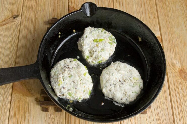 Shaping the farmer's cheese mixture into small patties and placing them in a hot pan. Shaped raw farmer's cheese patties being placed into a hot frying pan with oil.