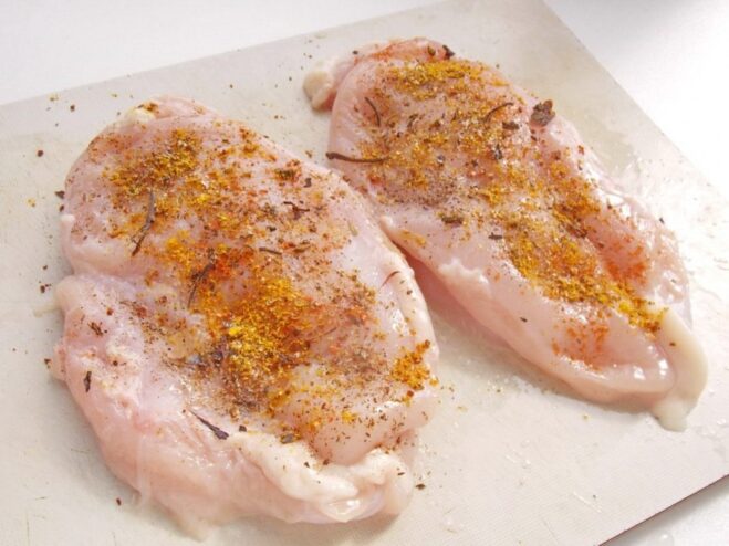 Marinating Chicken Breasts with Spices Raw chicken breasts in a bowl being rubbed with a mix of salt, pepper, and dried herbs.