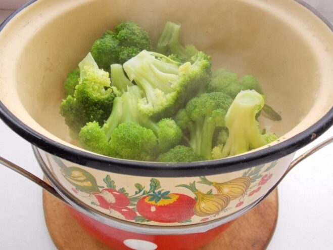 Draining the Blanched Broccoli in a Colander Bright green blanched broccoli florets in a white colander, with steam rising.