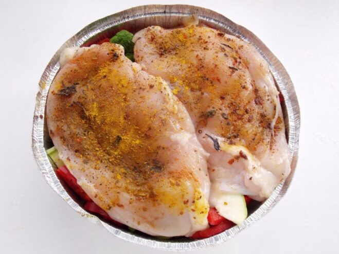 Placing Marinated Chicken on Top of the Vegetables Marinated raw chicken breasts being placed over the layer of mixed vegetables in a baking dish.