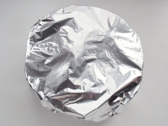 Covering the Baking Dish with Foil Before Baking The glass baking dish with chicken and vegetables being covered tightly with aluminum foil.