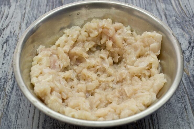 Hand-Chopped Chicken for Extra Juicy Cutlets Close-up of finely chopped raw chicken breast on a cutting board with a knife.