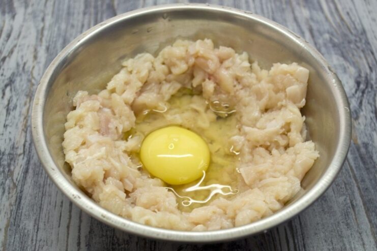 Binding the Ingredients with a Fresh Egg A raw egg cracked into a bowl of chopped chicken meat.