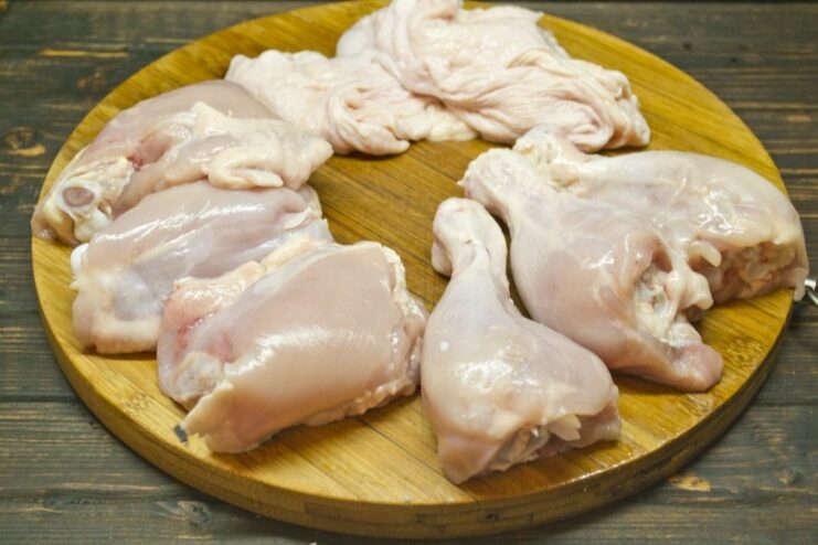 Hands deboning a chicken leg, carefully pulling the skin off in one piece.