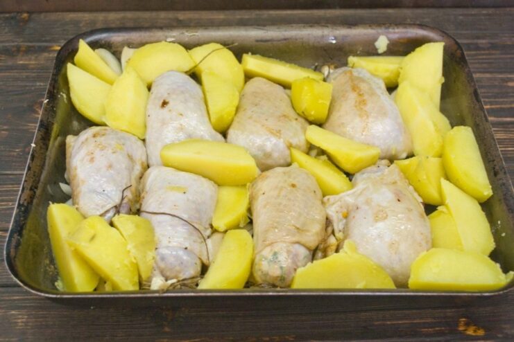 A baking dish with raw chicken cutlets, potato wedges, and onion rings, ready for the oven.