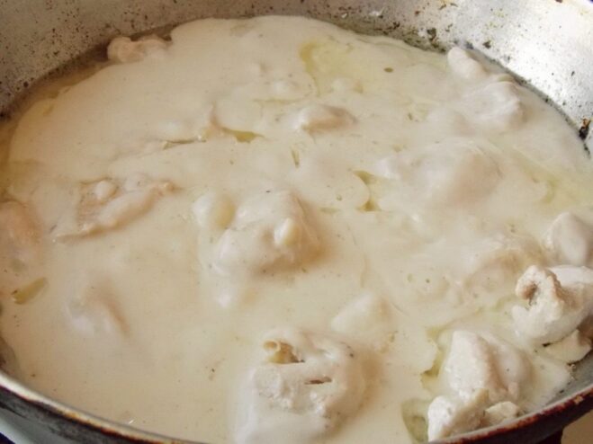 Combining the chicken and Béchamel sauce for the final simmer Pouring creamy Béchamel sauce over sautéed chicken pieces in a pan.