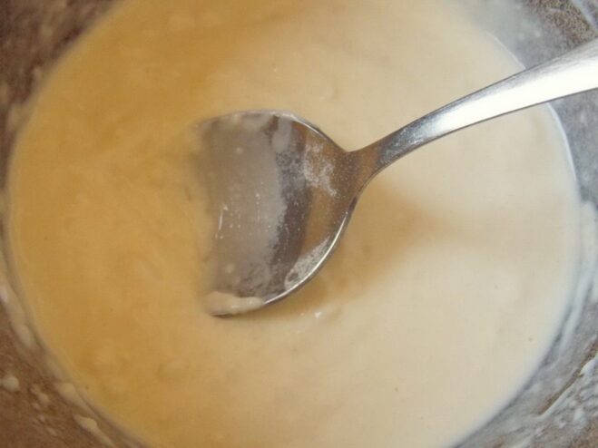Whisking the Béchamel sauce until smooth and creamy Whisking the white Béchamel sauce in a saucepan to remove lumps.