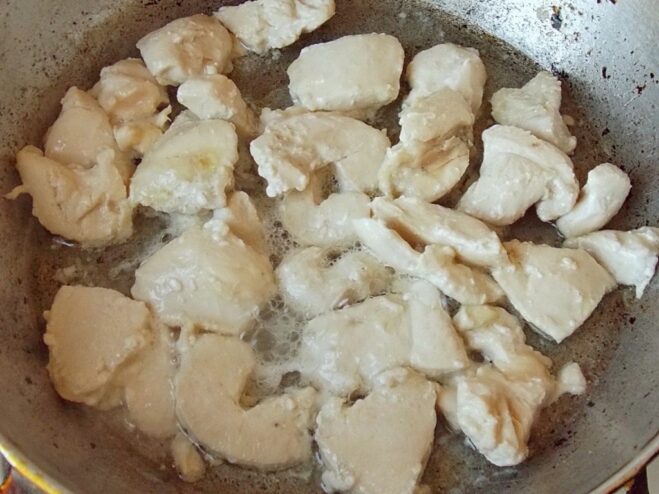 Sautéing chicken pieces until they turn white Pieces of raw chicken breast being sautéed in a hot frying pan.