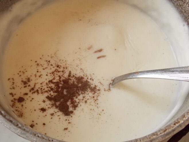 The secret ingredient: adding nutmeg to the Béchamel sauce A hand sprinkling ground nutmeg into a saucepan with white Béchamel sauce.