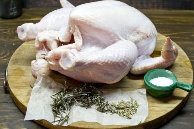 Seasoning the chicken inside and out for maximum flavor. Hands rubbing salt and spices onto the skin of a raw whole chicken.