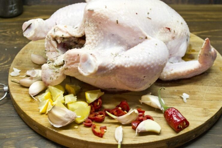 Aromatic stuffing: Filling the chicken cavity with lemon, chili, and garlic. A raw chicken cavity being stuffed with lemon wedges, chili, and garlic cloves.