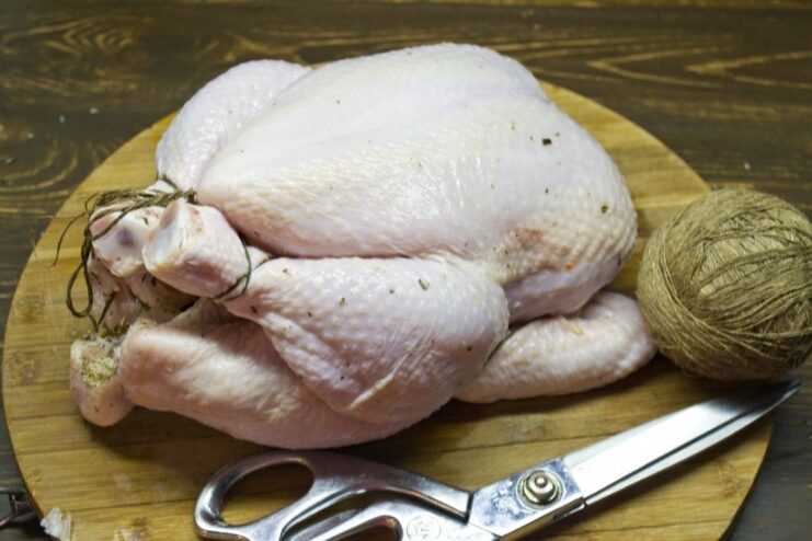 How to properly truss a chicken to ensure even cooking. A whole chicken being trussed with kitchen twine to secure the legs and wings.