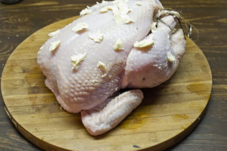 The secret to a golden crust: Brushing the chicken with melted butter. A hand brushing melted butter over the skin of a trussed whole chicken.