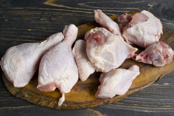 How to properly cut chicken leg quarters for even cooking. Raw chicken leg quarters being cut into thighs and drumsticks on a cutting board.