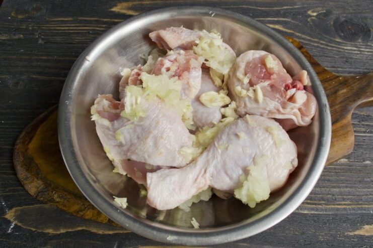 Seasoning chicken pieces with a fragrant onion and garlic paste. Chicken pieces in a bowl being rubbed with a minced onion and garlic mixture.