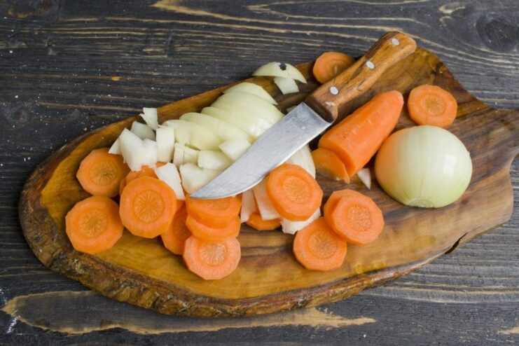 Preparing a bed of vegetables to place under the chicken for extra flavor and moisture. Thickly sliced rings of onion and rounds of carrot on a cutting board.