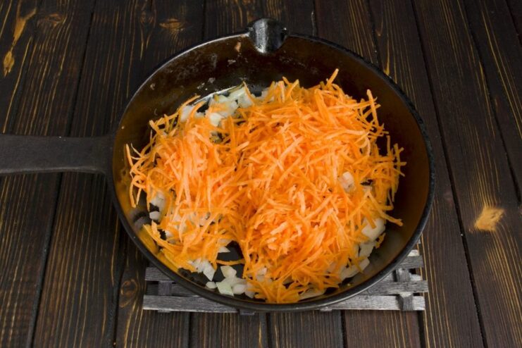 Adding Grated Carrots to the Sautéed Onions Grated carrots being sautéed with onions in a cast-iron skillet.