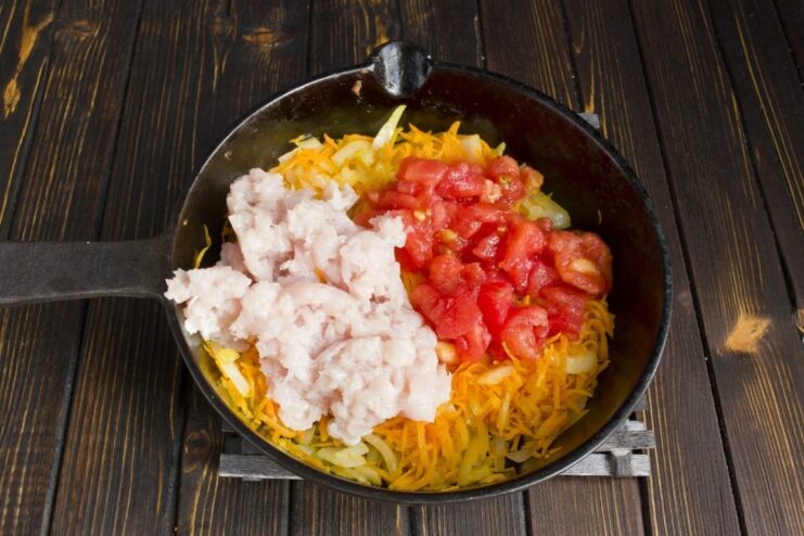 Browning Ground Chicken and Tomatoes with Vegetables Ground chicken and diced tomatoes being fried with sautéed onions and carrots in a skillet.