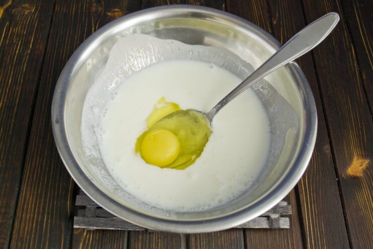 Preparing the Corn Pancake Batter: Whisking Egg and Prostokvasha An egg and prostokvasha (fermented milk) being whisked together in a deep bowl.