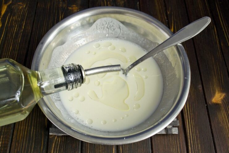 Adding Oil to the Pancake Batter for Tenderness Vegetable oil being poured into the egg and prostokvasha mixture for the pancake batter.