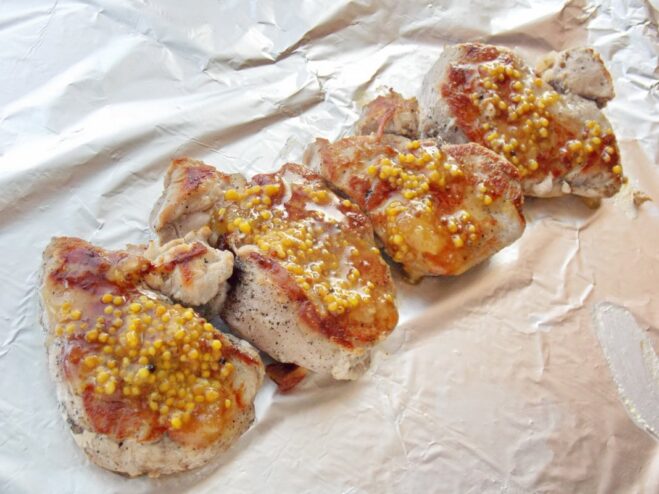 Step 4: Glazing the seared pork with honey-mustard sauce Seared pork medallions on a sheet of aluminum foil being brushed with honey-mustard sauce.