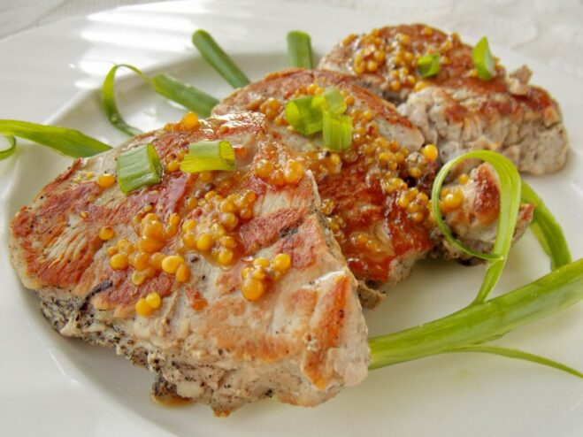 A plate of finished pork medallions in honey-mustard sauce, garnished with fresh herbs.