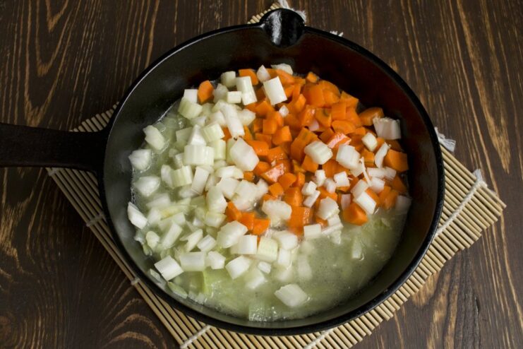 Adding carrots, celery, and broth to the sautéed onions to build the flavor base. Chopped carrots and celery being added to the pan with sautéed onions.