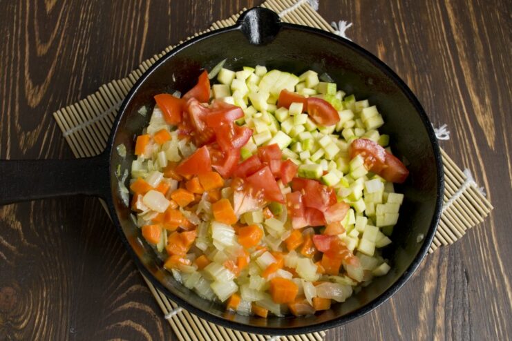 Adding fresh zucchini and tomatoes to the vegetable mix for extra flavor and texture. Diced zucchini and tomatoes being added to the simmering vegetables in the pan.