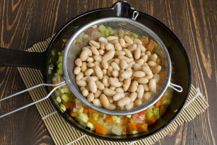 Rinsing canned beans before adding them to the ragout to remove excess salt. Canned white beans being drained in a colander before being added to the vegetable stew.