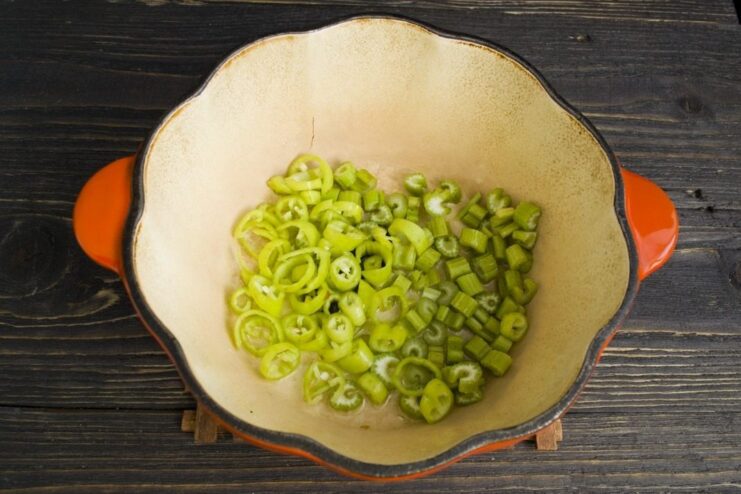 Sautéing aromatics to build the flavor base for the stew Chopped celery and a hot pepper pod being sautéed in a Dutch oven.