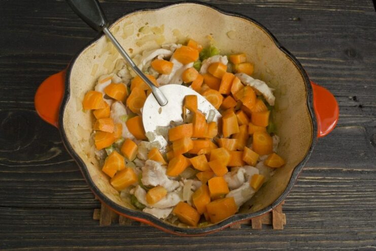 Adding diced carrots to the stew Diced carrots being sautéed with chicken and other vegetables in the pot.