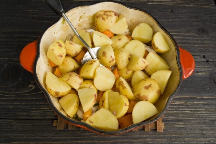 Adding large chunks of potato to make the stew hearty Large chunks of potato being added to the other ingredients in the Dutch oven.