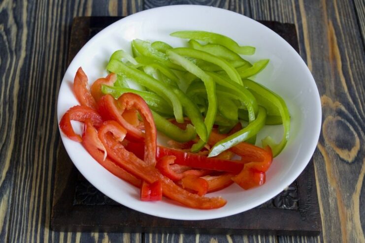 Slicing bell peppers into thin strips for the recipe Red bell pepper being sliced into thin strips.