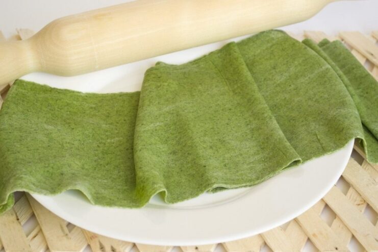 Step 6: Rolling out the rested dough into a thin sheet. Rolling out the green spinach pasta dough with a wooden rolling pin.