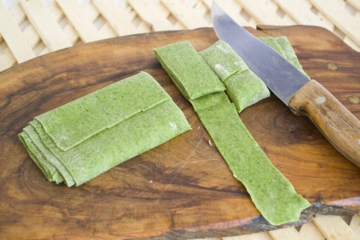 Step 7: Cutting the rolled dough into pasta strips. A rolled-up sheet of green pasta dough being sliced into noodles.
