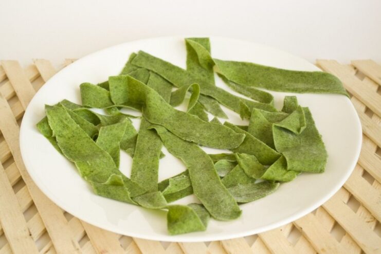 Step 8: Lightly drying the freshly cut pasta before cooking. Freshly cut green spinach pasta noodles spread out on a surface dusted with semolina.
