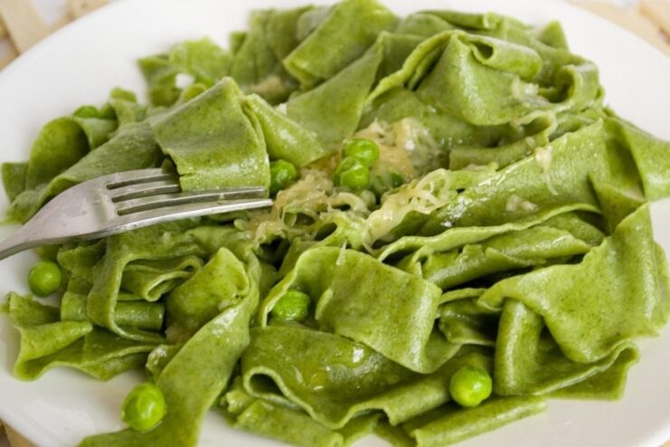 Final touch: Garnish with cheese and serve immediately for the best taste. A forkful of homemade spinach pasta being lifted from a plate, topped with grated cheese.