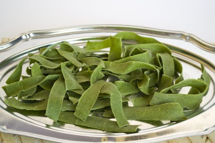 A method for drying homemade pasta for longer storage. Fresh spinach pasta noodles laid out on a tray dusted with semolina to dry.