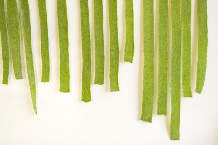 An alternative method for drying pasta by hanging it. Strands of fresh green spinach pasta hanging from a clothes hanger to dry.