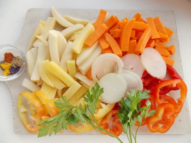 Sliced raw potatoes, pumpkin, onion, and bell peppers in a bowl, ready for cooking.