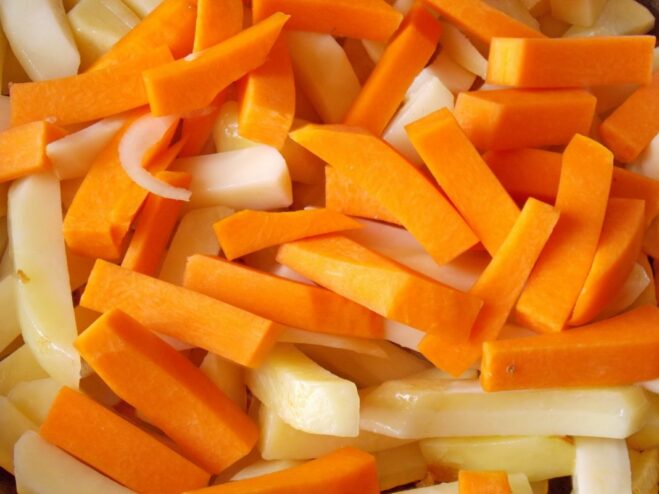 Pieces of pumpkin being added to the skillet with the pan-frying potatoes.