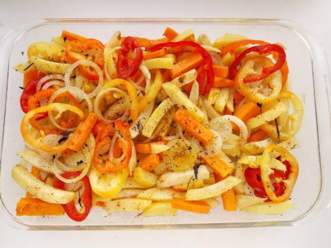 The mixture of pan-fried potatoes, pumpkin, and other vegetables being transferred to a glass baking dish.