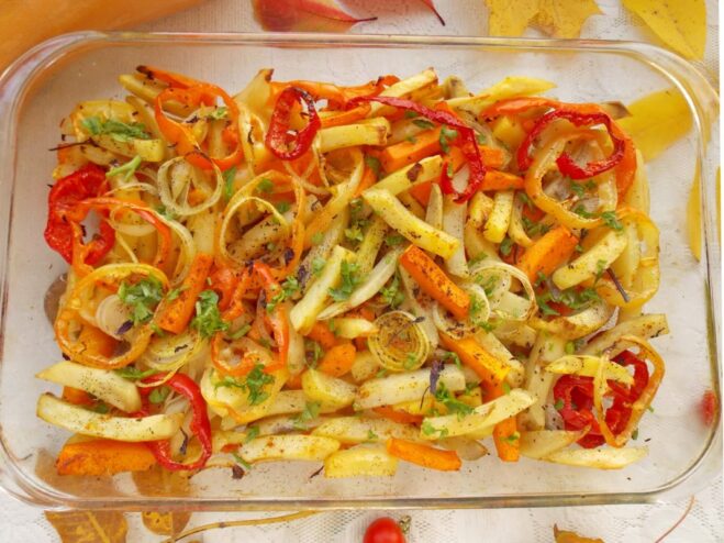 The glass baking dish with potatoes, pumpkin, and vegetables baking inside a hot oven.