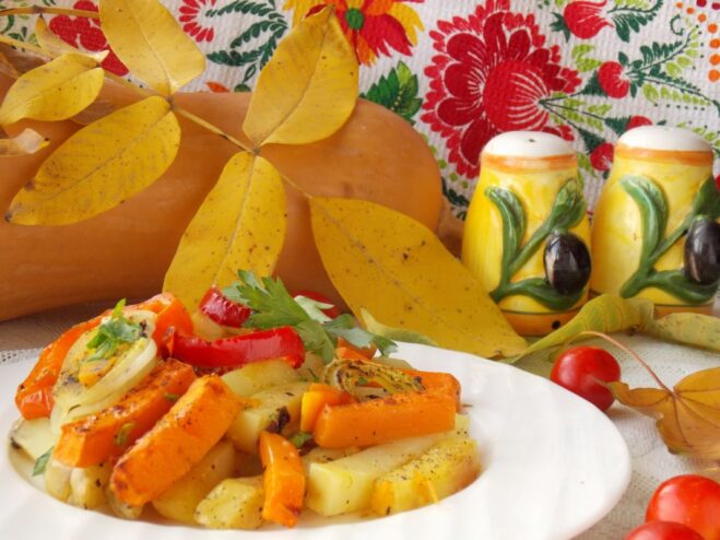 A serving of the finished oven-baked potatoes with pumpkin and vegetables in a white bowl, garnished with fresh herbs.