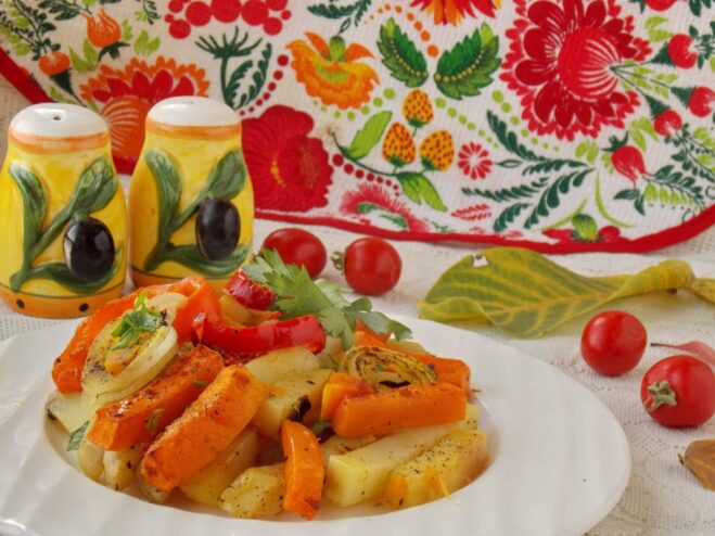 A close-up shot of a bowl of oven-baked potatoes, pumpkin, and vegetables, garnished with fresh herbs.