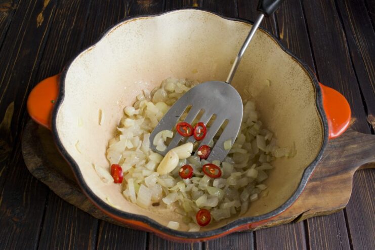 Sautéing onions and chili peppers to build the aromatic base for the plov. Chopped onions and chili rings being sautéed in a dutch oven.